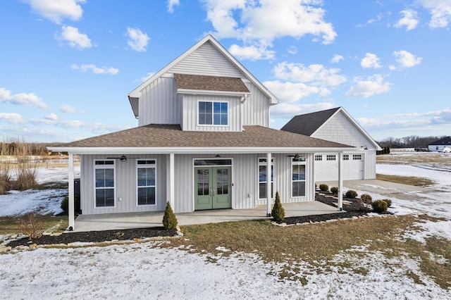 snow covered back of property featuring a garage, french doors, and covered porch