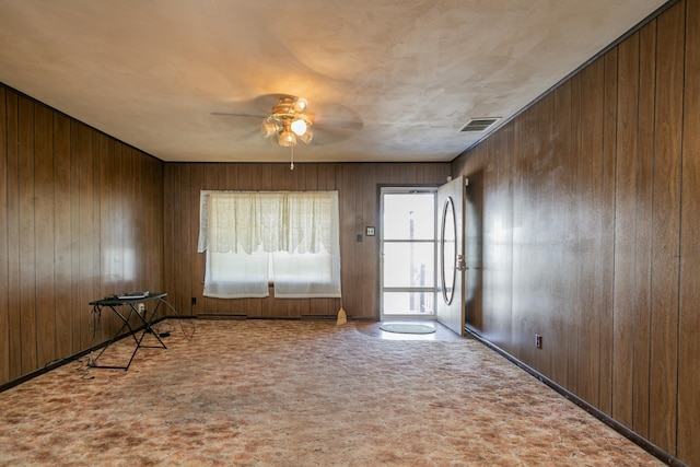 interior space featuring ceiling fan, light colored carpet, and wood walls