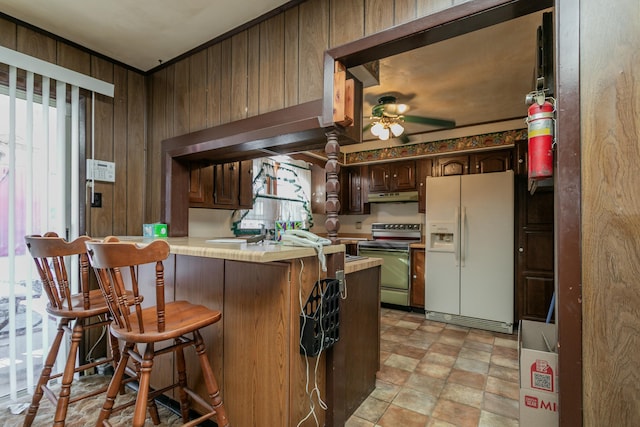 kitchen featuring electric stove, white refrigerator with ice dispenser, wooden walls, and plenty of natural light