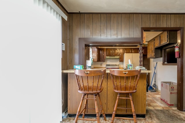 kitchen with stove, white refrigerator with ice dispenser, a kitchen bar, kitchen peninsula, and wood walls