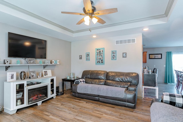 living room with crown molding, a raised ceiling, and light hardwood / wood-style floors