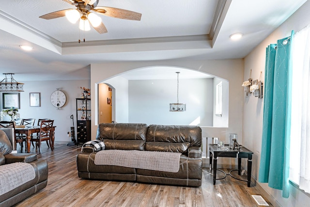 living room featuring ceiling fan, ornamental molding, a raised ceiling, and hardwood / wood-style floors