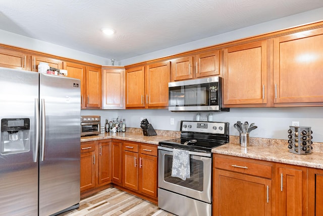 kitchen featuring light hardwood / wood-style flooring, light stone countertops, and appliances with stainless steel finishes