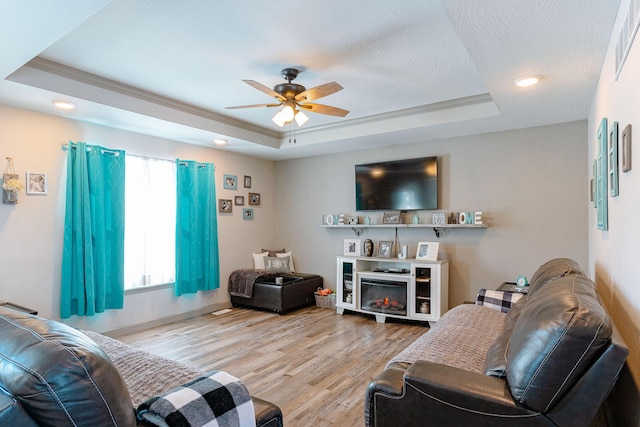 living room with ornamental molding, a raised ceiling, and light hardwood / wood-style flooring