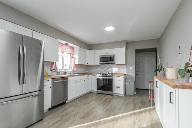 kitchen featuring butcher block counters, white cabinets, decorative backsplash, stainless steel appliances, and light wood-type flooring