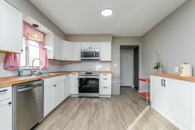 kitchen featuring butcher block countertops, sink, light hardwood / wood-style flooring, white cabinetry, and stainless steel appliances