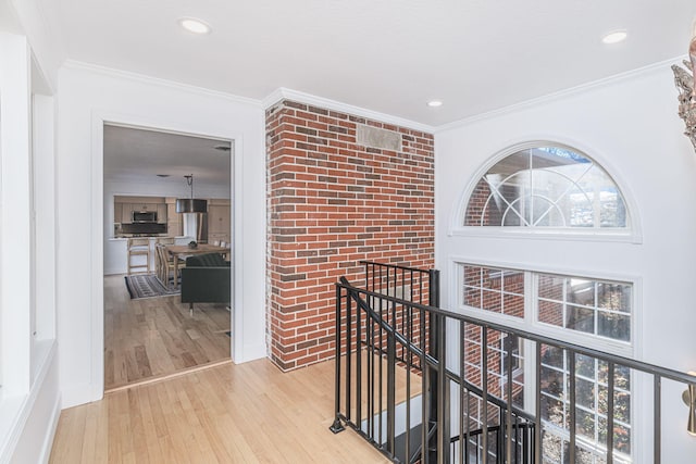 hallway with brick wall, ornamental molding, and light wood-type flooring