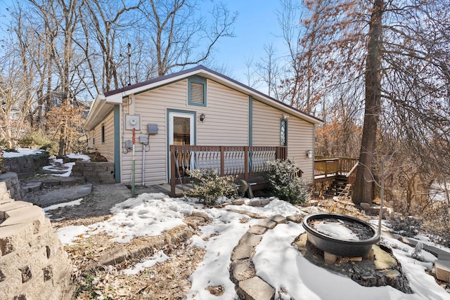 snow covered rear of property with a deck and a fire pit