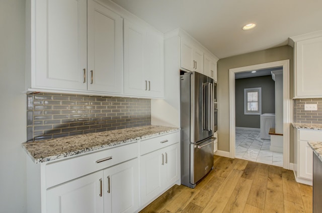 kitchen featuring white cabinetry, light stone counters, high end refrigerator, light wood-type flooring, and backsplash