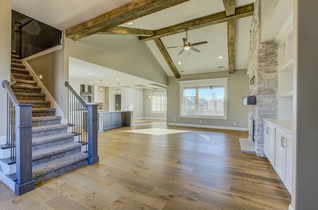 unfurnished living room with sink, light wood-type flooring, beamed ceiling, ceiling fan, and a fireplace