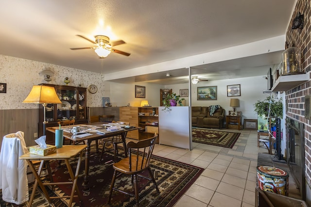 dining area featuring ceiling fan, a fireplace, wood walls, and light tile patterned floors