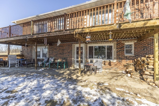 snow covered back of property featuring a wooden deck and a patio area