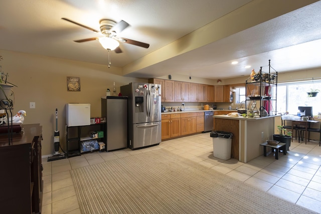 kitchen with a breakfast bar, ceiling fan, appliances with stainless steel finishes, a center island, and light tile patterned flooring