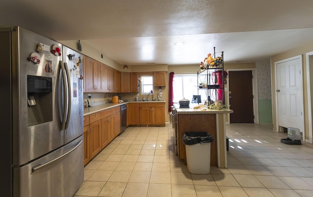 kitchen with stainless steel appliances, sink, light tile patterned floors, and a textured ceiling