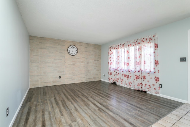 unfurnished room with hardwood / wood-style floors and brick wall