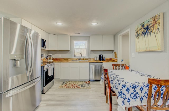 kitchen with appliances with stainless steel finishes, wood counters, white cabinetry, sink, and a textured ceiling