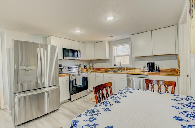 kitchen featuring sink, wooden counters, appliances with stainless steel finishes, light hardwood / wood-style floors, and white cabinets