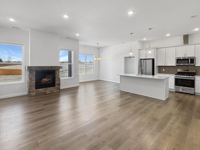 kitchen with a kitchen island with sink, white cabinetry, stainless steel appliances, light hardwood / wood-style floors, and decorative light fixtures