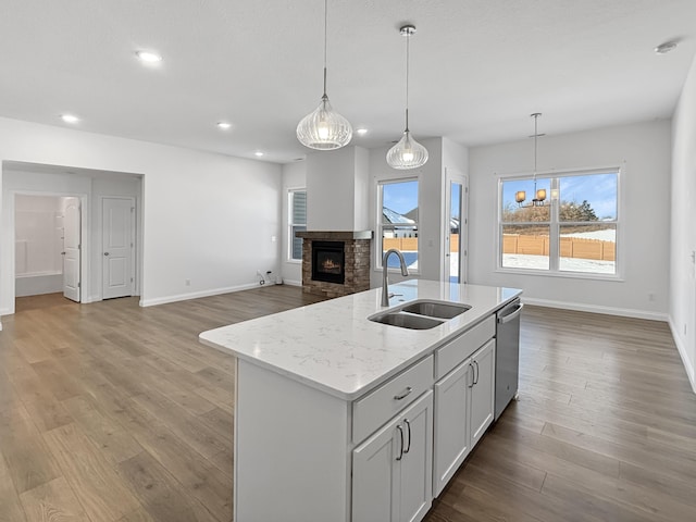 kitchen featuring dishwasher, sink, hanging light fixtures, a kitchen island with sink, and light stone countertops