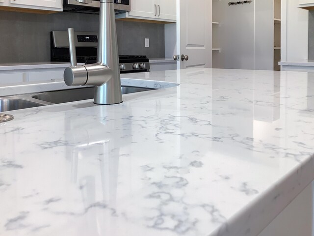 interior details with light stone counters, sink, and white cabinets