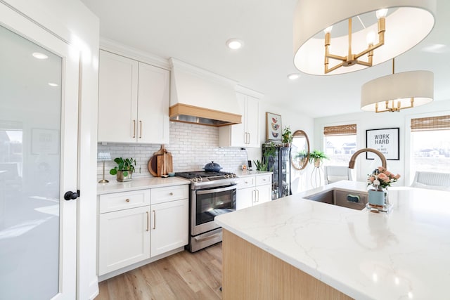 kitchen with white cabinetry, decorative light fixtures, custom exhaust hood, and stainless steel gas range oven