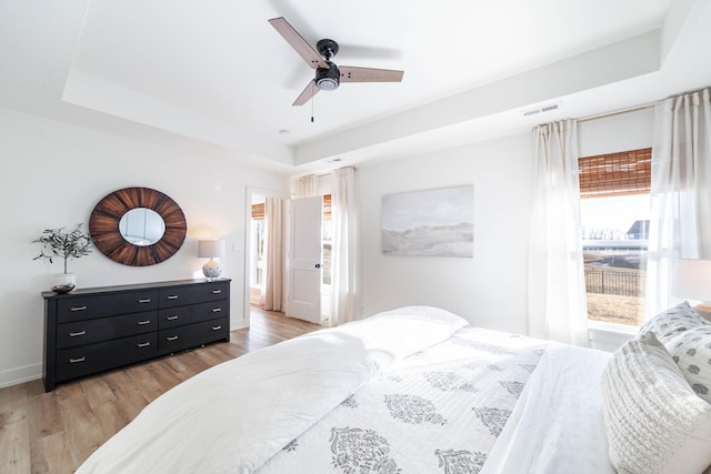 bedroom with ceiling fan, a tray ceiling, and light hardwood / wood-style flooring