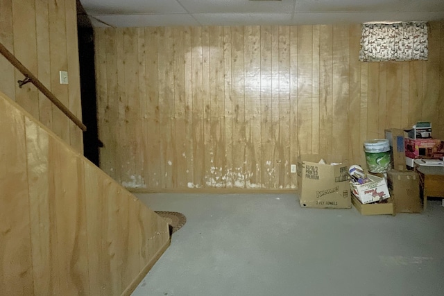 basement featuring a paneled ceiling and wood walls