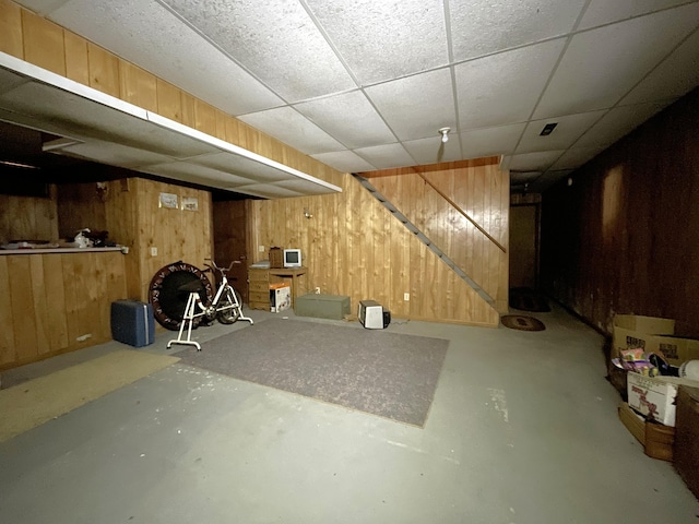 basement featuring a paneled ceiling and wood walls