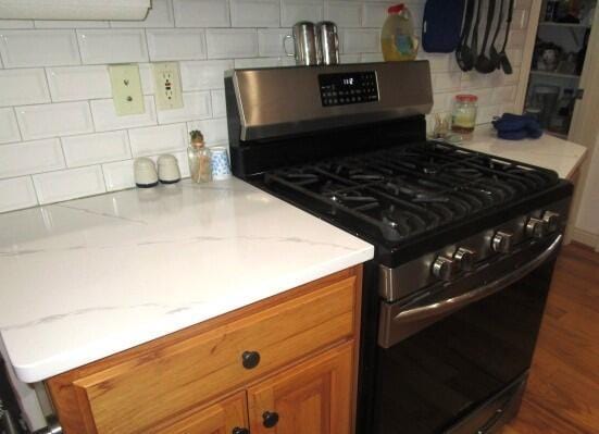 kitchen with tasteful backsplash, gas stove, and light stone countertops