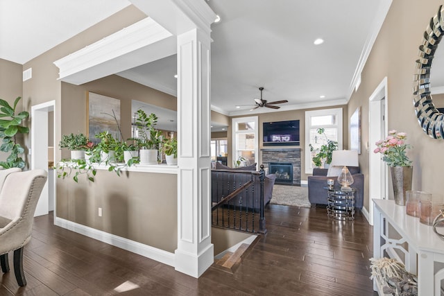 interior space with ornate columns, a stone fireplace, dark hardwood / wood-style flooring, ornamental molding, and ceiling fan