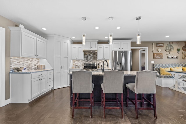 kitchen featuring appliances with stainless steel finishes, hanging light fixtures, light stone counters, white cabinets, and a center island with sink