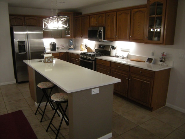 kitchen featuring light tile patterned floors, a breakfast bar area, stainless steel appliances, a kitchen island, and decorative light fixtures