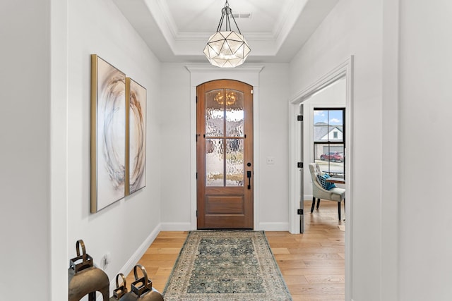 foyer entrance featuring crown molding, a raised ceiling, an inviting chandelier, and light wood-type flooring