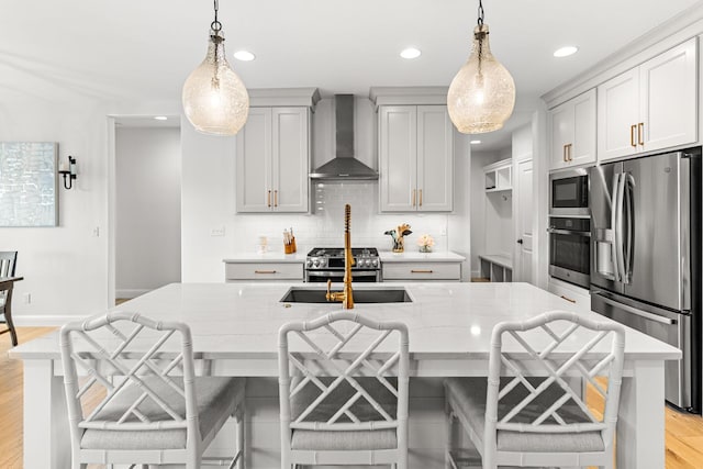 kitchen with hanging light fixtures, appliances with stainless steel finishes, a breakfast bar area, and wall chimney range hood