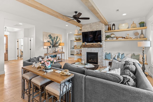 living room with beamed ceiling, ceiling fan, a fireplace, and light hardwood / wood-style floors