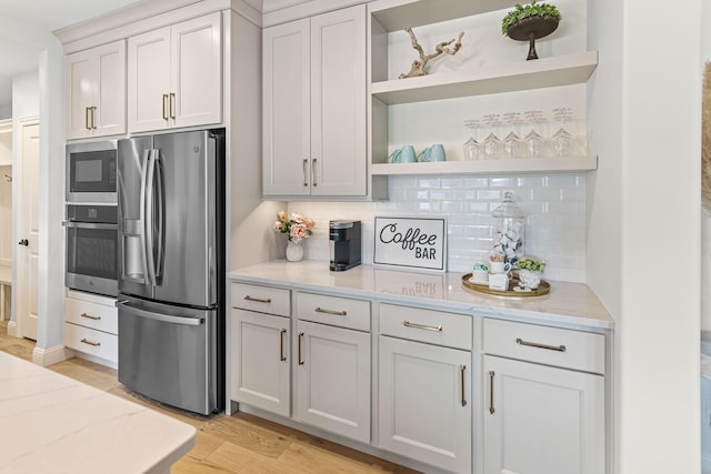 kitchen featuring white cabinetry, light wood-type flooring, appliances with stainless steel finishes, light stone countertops, and backsplash