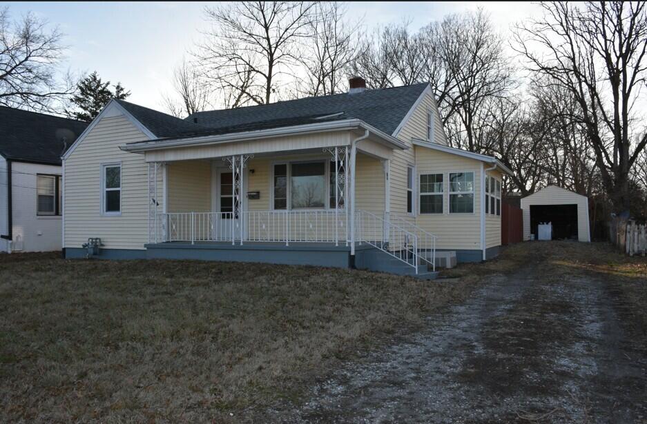 view of front of house featuring a garage, an outdoor structure, covered porch, and a front lawn