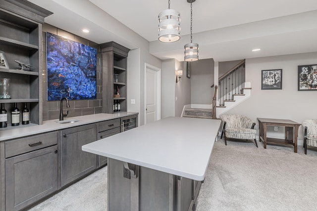 kitchen featuring sink, a center island, light carpet, hanging light fixtures, and beverage cooler