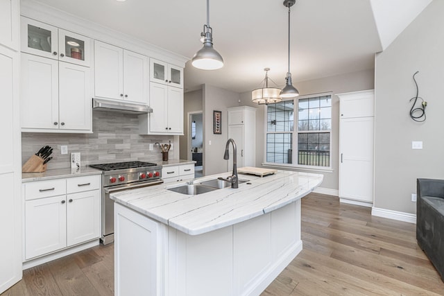 kitchen featuring sink, high end stainless steel range oven, white cabinetry, light stone counters, and an island with sink