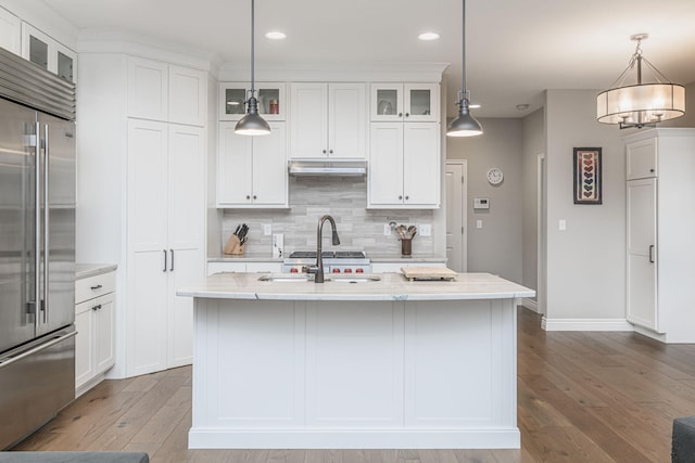 kitchen with hanging light fixtures, sink, an island with sink, and built in refrigerator