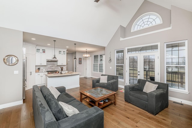 living room featuring french doors, an inviting chandelier, high vaulted ceiling, and light wood-type flooring