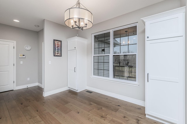 unfurnished dining area featuring an inviting chandelier and hardwood / wood-style floors