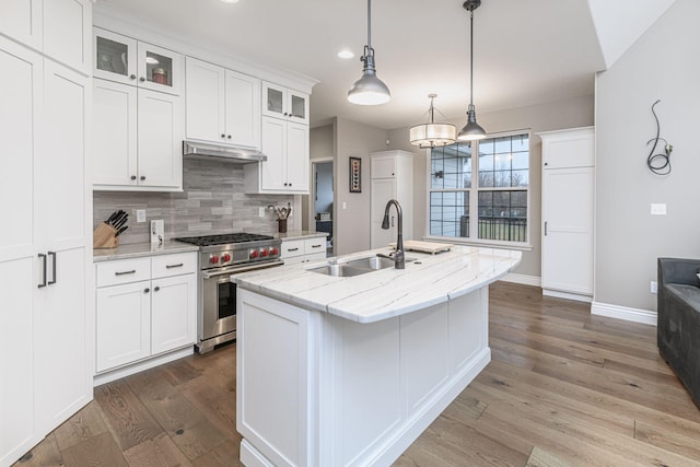 kitchen with light stone counters, high end stove, white cabinets, and a center island with sink