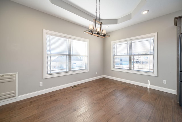 empty room with a notable chandelier, dark wood-type flooring, and a raised ceiling