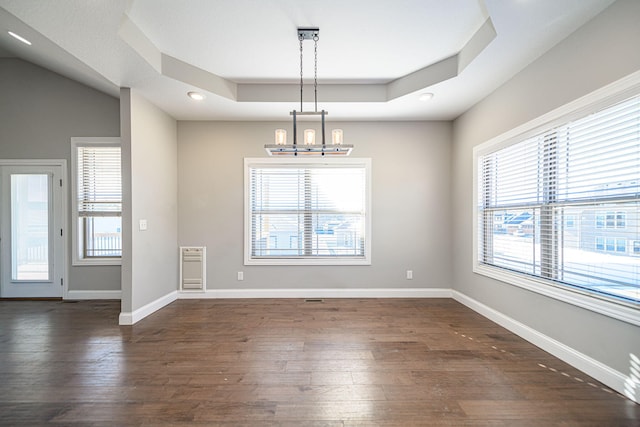 unfurnished dining area featuring dark hardwood / wood-style floors, a tray ceiling, and a chandelier