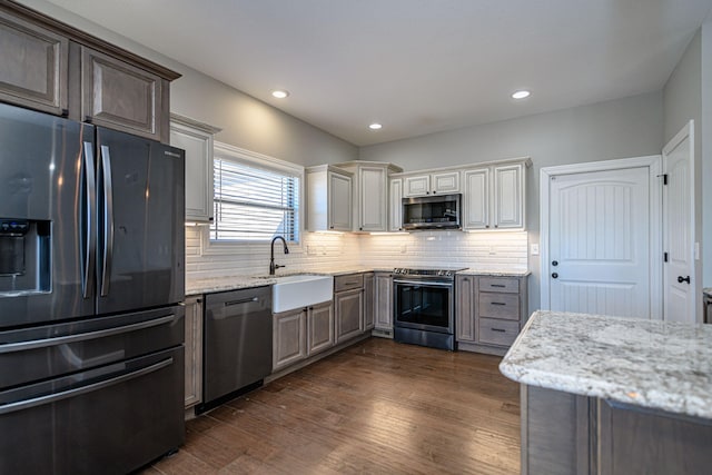 kitchen featuring sink, tasteful backsplash, light stone counters, appliances with stainless steel finishes, and dark hardwood / wood-style flooring