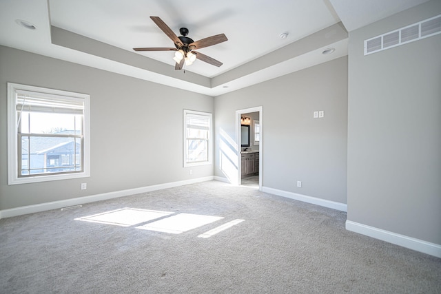 unfurnished room featuring a tray ceiling, light colored carpet, and ceiling fan