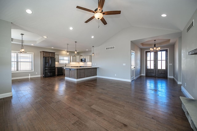 unfurnished living room with dark hardwood / wood-style floors, a wealth of natural light, a raised ceiling, and ceiling fan with notable chandelier