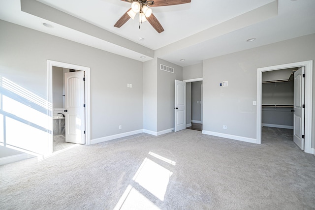 unfurnished bedroom featuring light carpet, a spacious closet, a closet, and ceiling fan