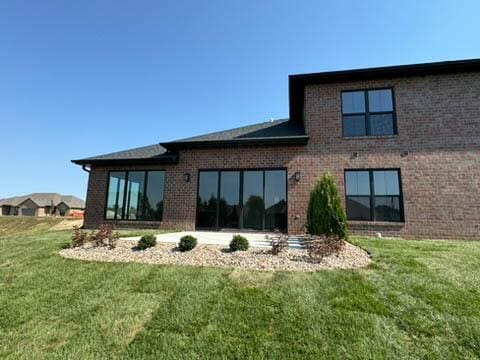 back of property with a lawn and brick siding